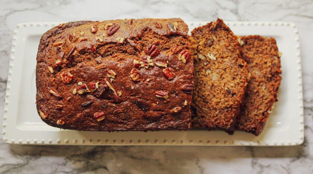 Banana bread loaf slices on a white platter on a marble counter