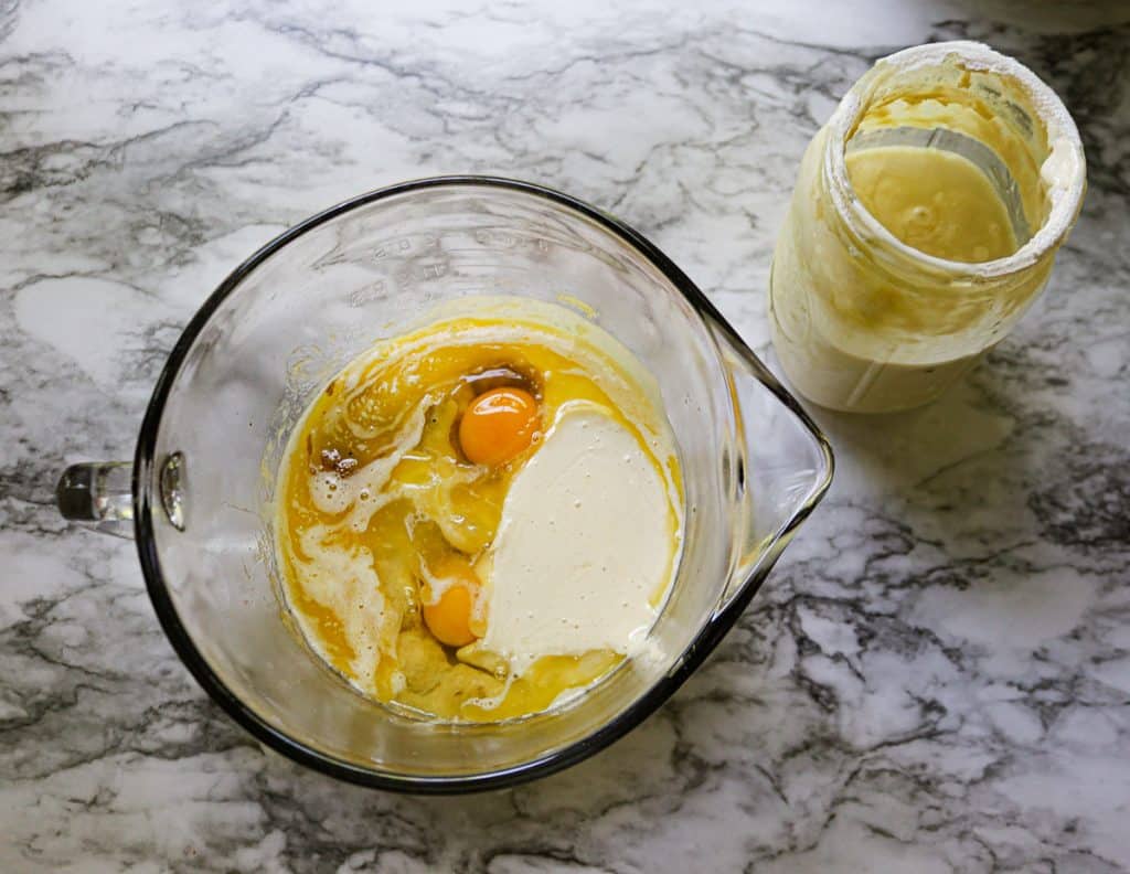 eggs, sourdough starter and mashed bananas in a glass bowl on a marble counter with a jar of sourdough starter