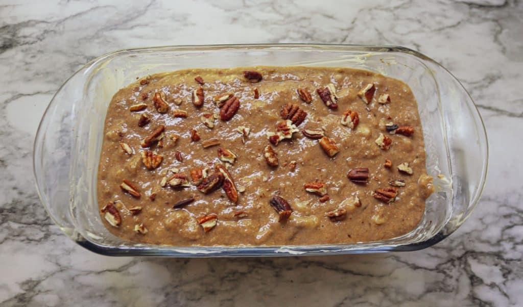 unbaked banana bread with pecans on top in a glass loaf pan on a marble counter