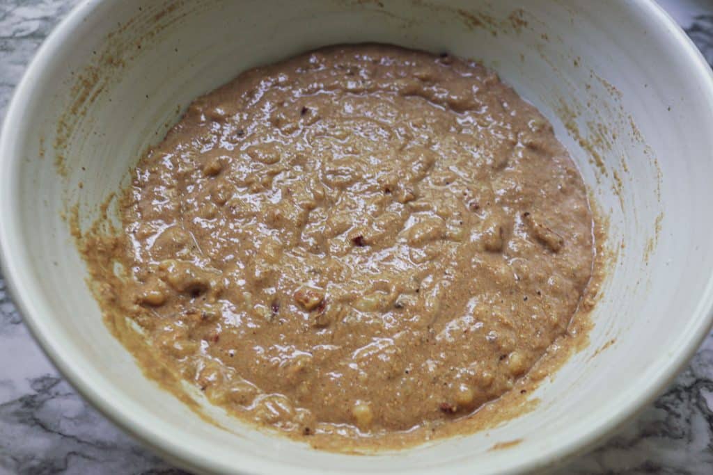 wet banana bread batter in white bowl on a white marble counter