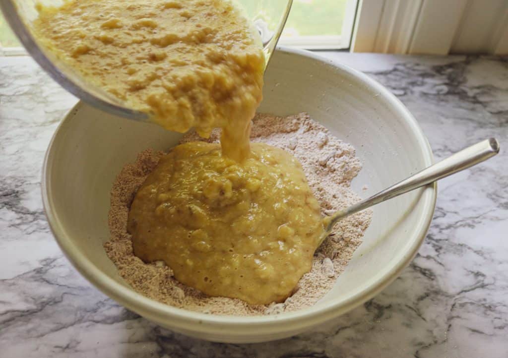 adding wet ingredients to dry ingredients in a white bowl on a white marble counter