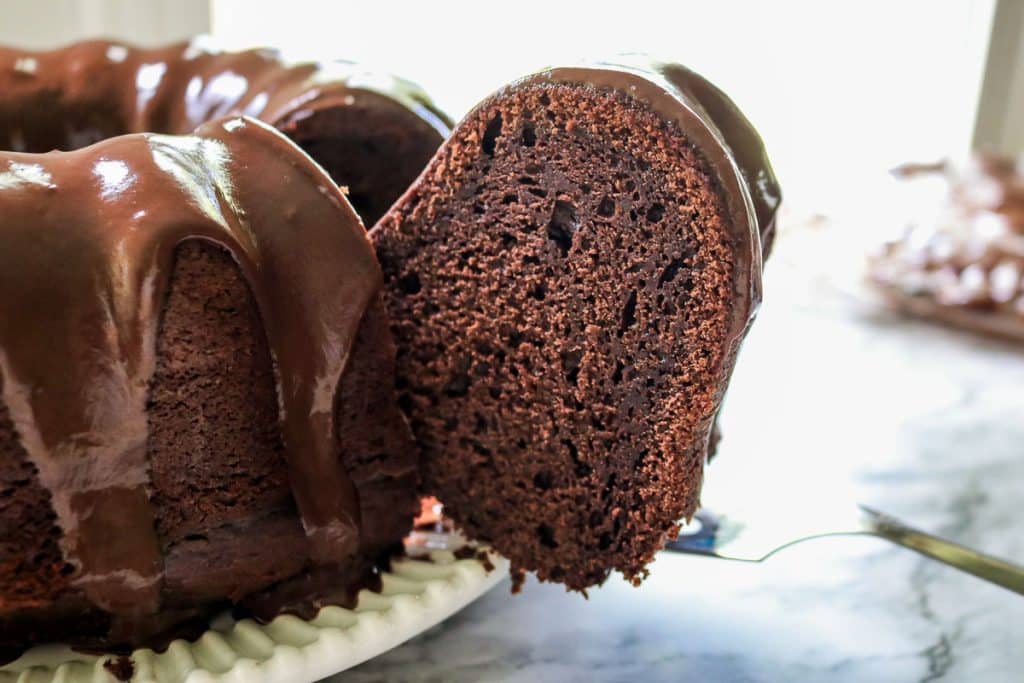a slice being lifted out of a chocolate sourdough pound cake by a metal spatula on a white plate