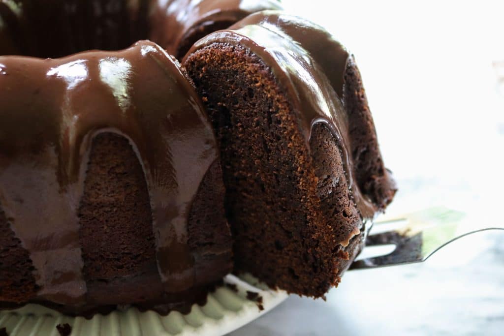 a slice being lifted out of a chocolate sourdough pound cake by a metal spatula on a white plate