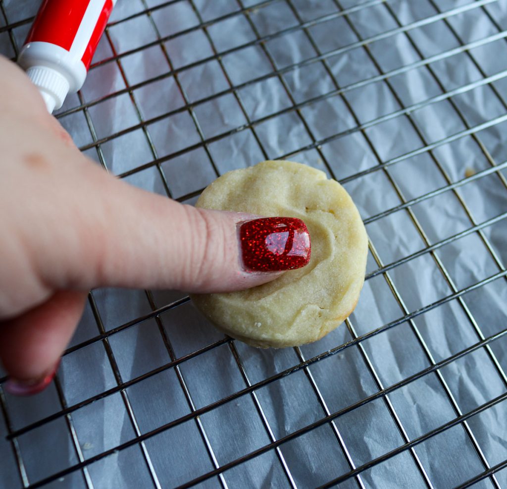 a thumb pressing into cookie dough on a wire rack