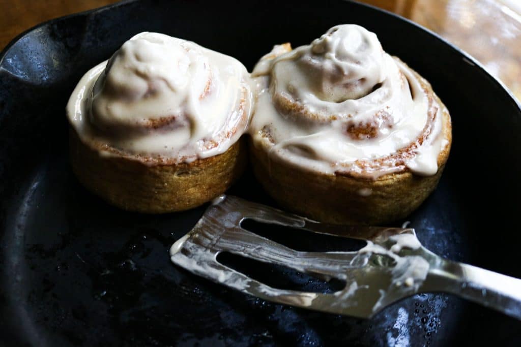 two cinnamon rolls in a cast iron pan with a spatula