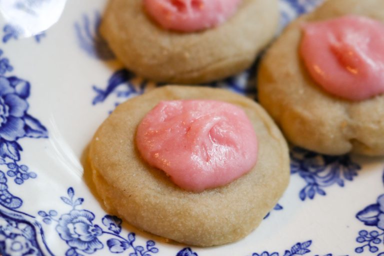 a small bite sized sourdough shortbread tea cookie with pink icing on a white and blue plate