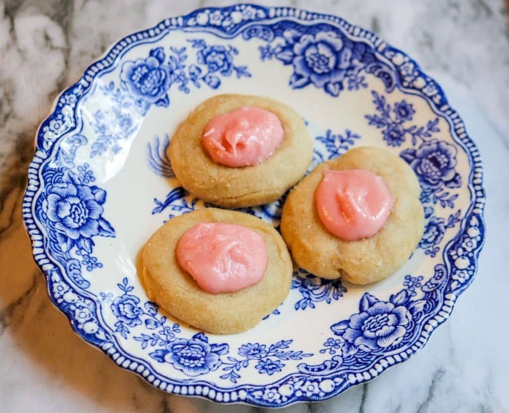 a small bite sized sourdough shortbread tea cookie with pink icing on a white and blue plate