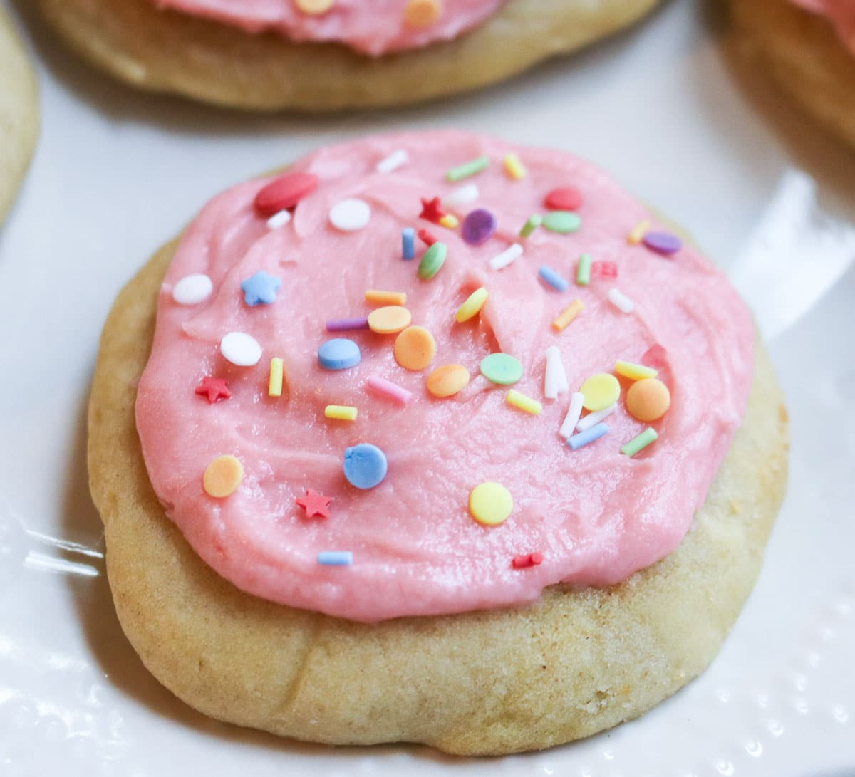 pink iced sugar cookies with sprinkles on parchment