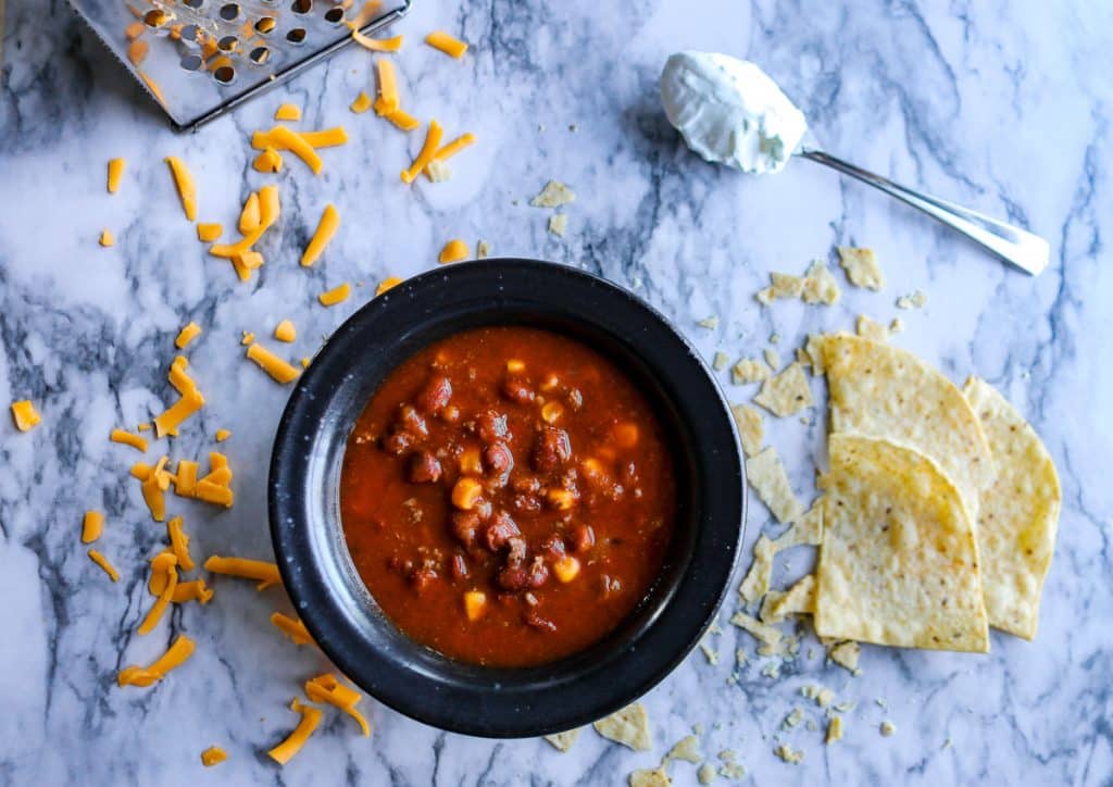 black bowl of taco soup on a white marble counter with a spoon of sour cream on the counter