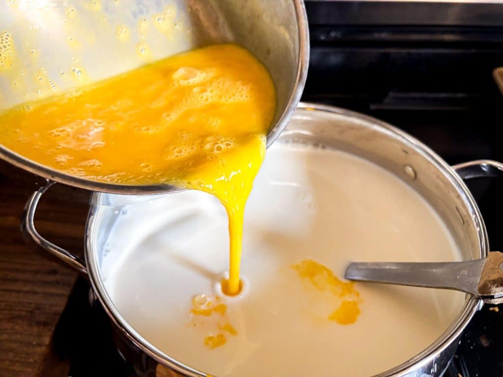 pouring egg mix into milk in a stainless steel pot