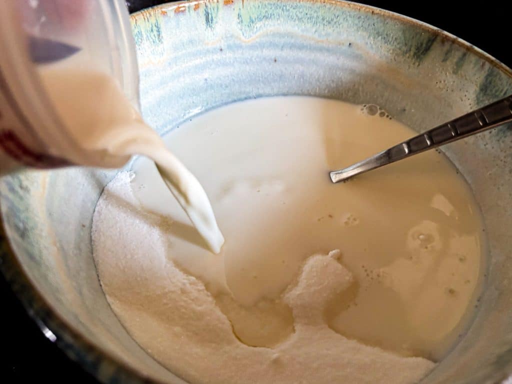 adding milk to sugar and cornstarch in a light blue pottery bowl