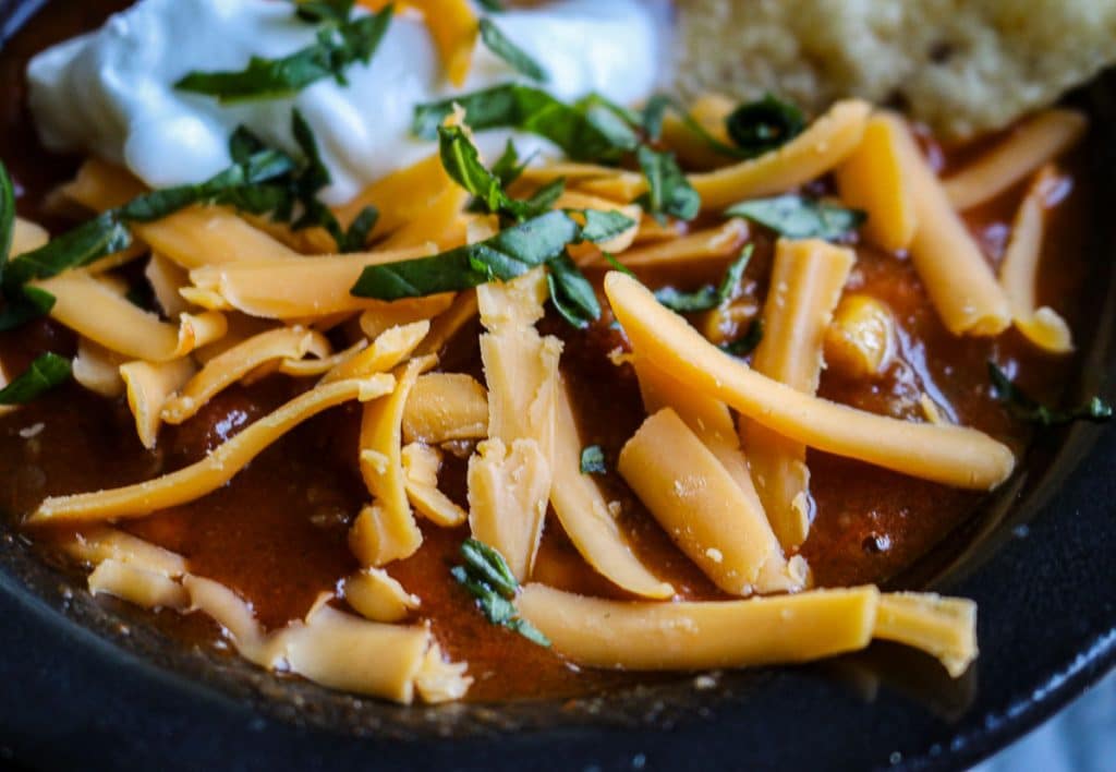 upclose toppings of sour cream, cheese and tortilla chips in a black bowl of taco soup