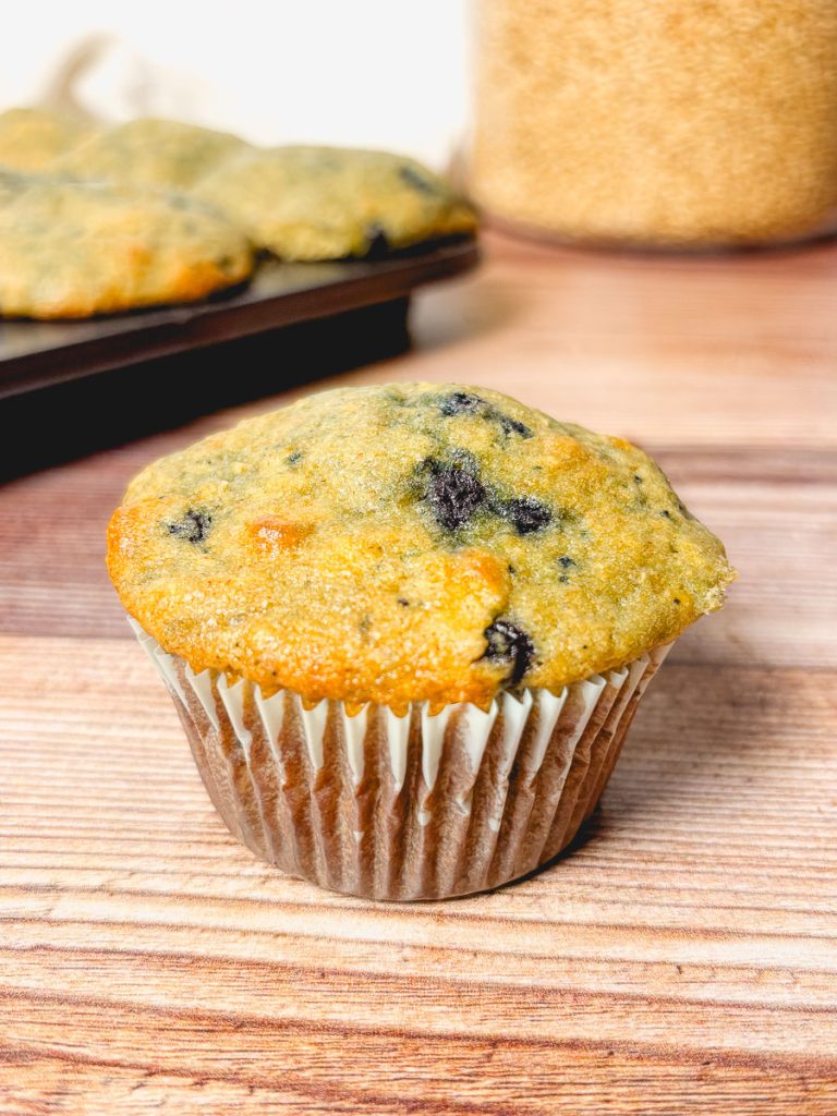 a blueberry muffin make with whole grains in front of a jar of whole wheat berries