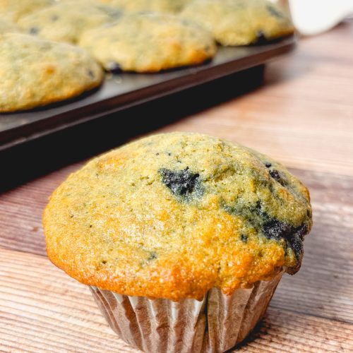 a blueberry muffin make with whole grains in front of a full tray of muffins