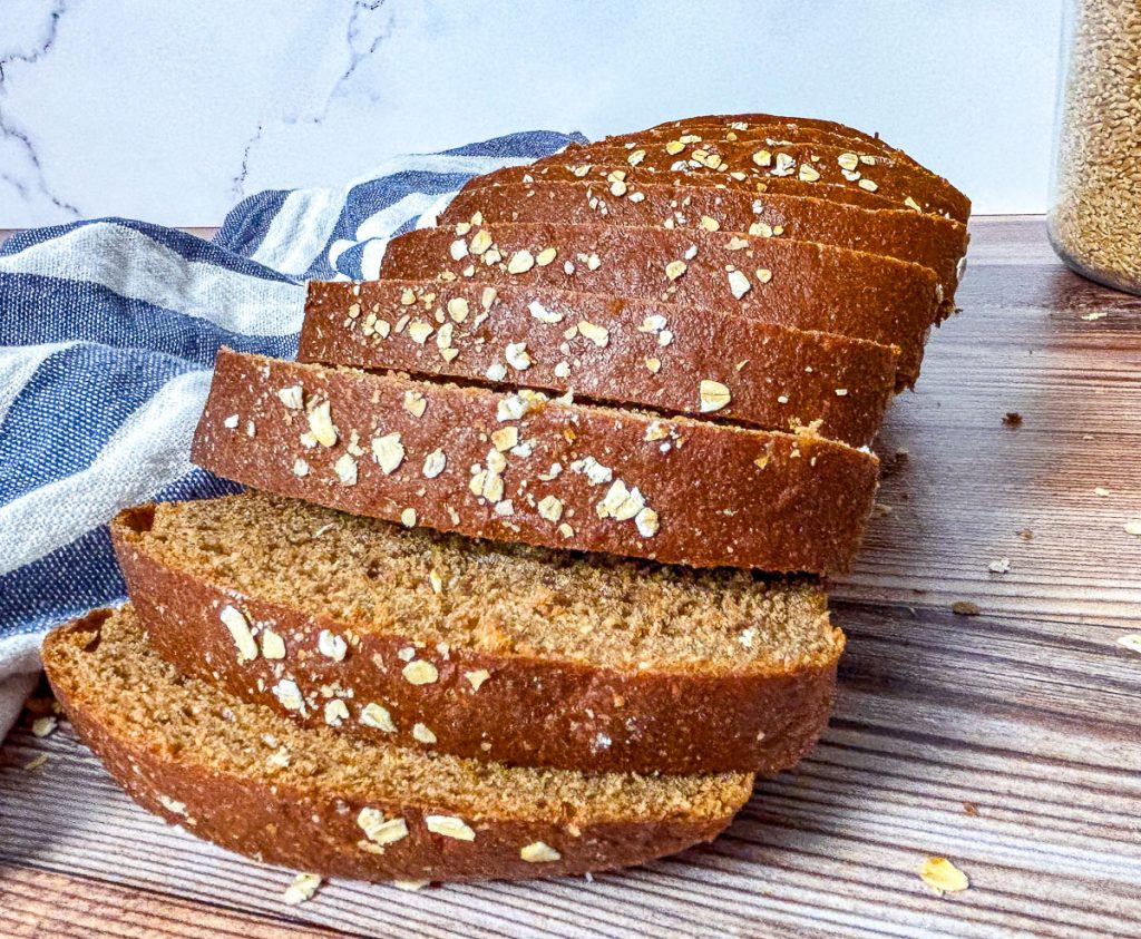 slices of brown bread made with fresh milled flour and topped with oats, a blue and white tea towel in the background