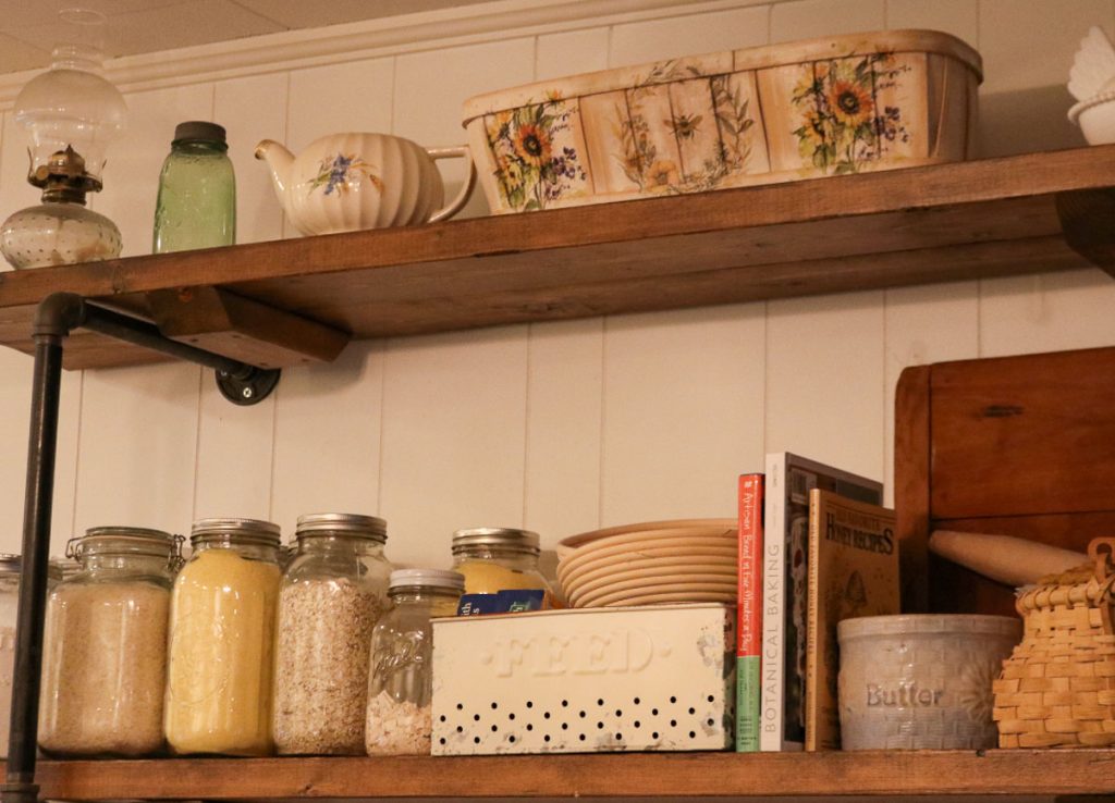Organized from scratch pantry with glass jars of flour and oats, cookbooks, bread baskets, and everyday baking essentials on wooden shelves.