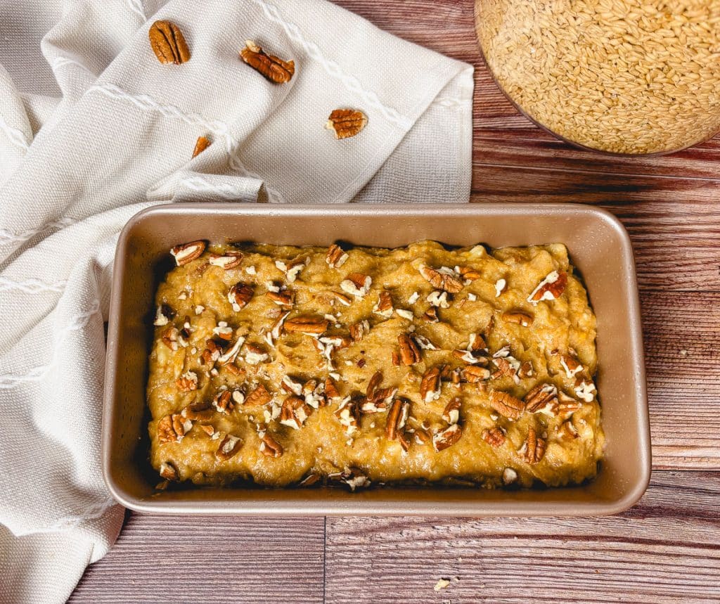 Banana bread batter topped with chopped pecans spread in a loaf pan before baking.