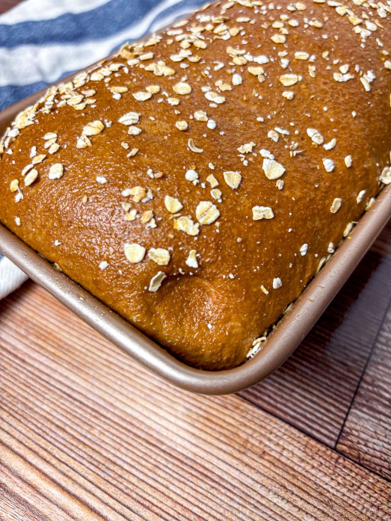 brown bread loaf with oat topping with an indent showing that it is proofed