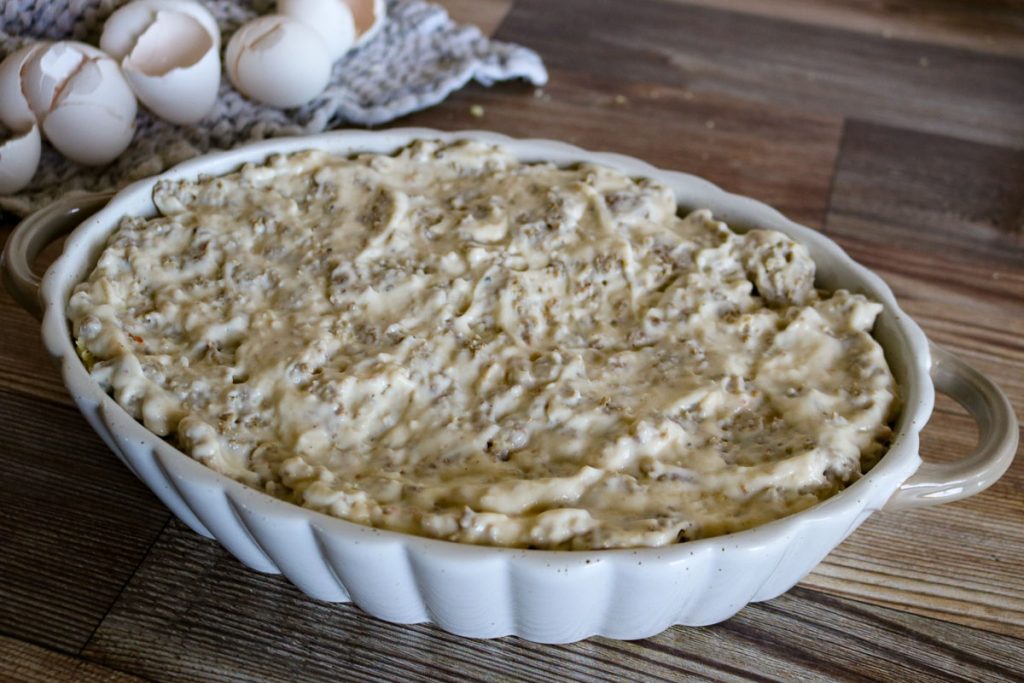 Unbaked sourdough breakfast casserole with sausage gravy and eggs in background