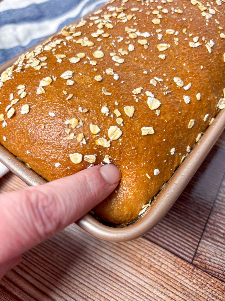 a finger poking brown bread dough to see if its proof