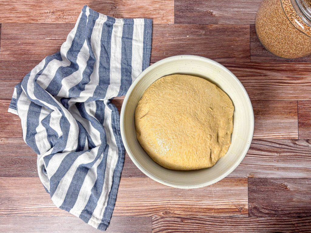 Freshly kneaded honey wheat dough resting in a white bowl before rising.