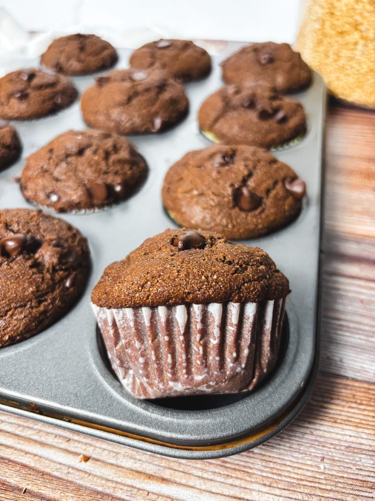 a tray full of baked double chocolate chip muffins with one muffin turned on its side